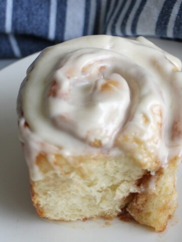 Single Cinnamon roll on a white plate with blue background.