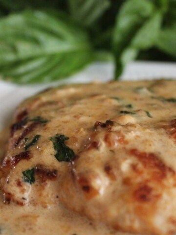 Sauteed chicken covered in cream gravy with a sprig of basil behind it.