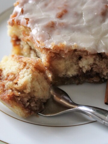 Fork full of cinnamon roll cake with a side of cinnamon sticks.