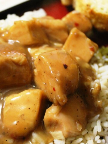 Close up of chicken covered with a shiny brown sauce, over rice.