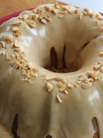 Peanut butter bundt cake dripping with frosting and topped with chopped nuts.