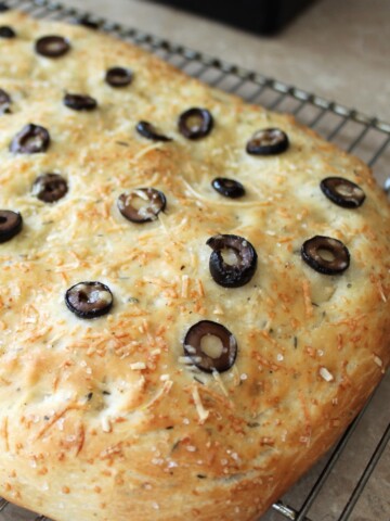 Focaccia bread with black olives and cheese on a cooling rack.