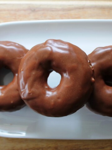 Three chocolate covered cake donuts on a white plate.