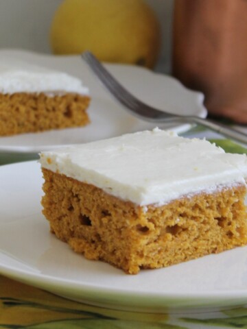 Slice of pumpkin cake with lemon cream cheese frosting on a white plate with lemon in the background.