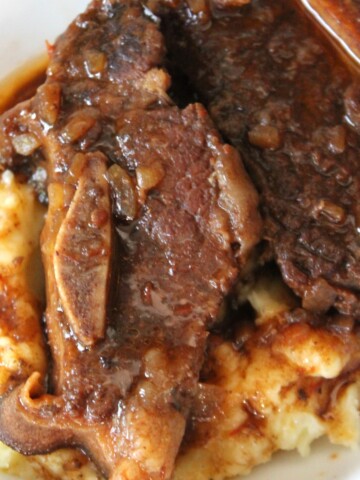 Close up of beef ribs in sauce over mashed potatoes.