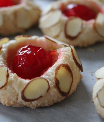 Little chewy almond paste cookies with a maraschino cherry in the center, dotted with sliced almonds.