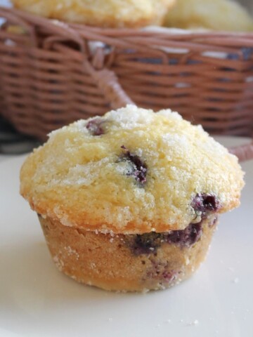 Muffins dotted with blueberries on a white plate with a basket in the background.
