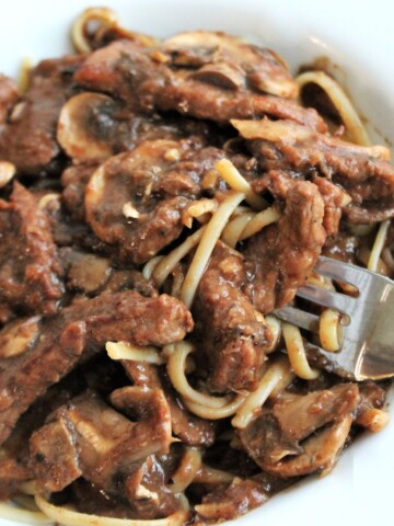 Close up view of a bowl of beef burgundy, mushrooms, and pasta.