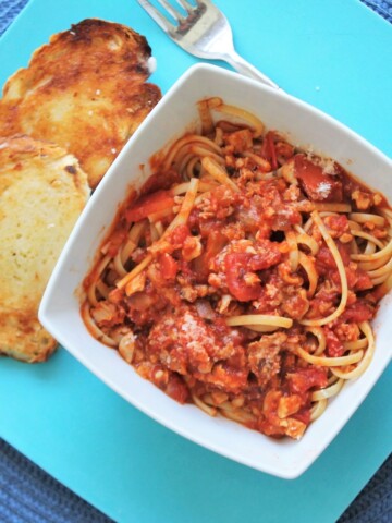 Overhead view of a bowl of linguine with red clam sauce on a blue plate with garlic bread on the side.
