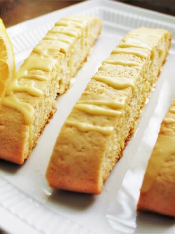 Close up of three lemon biscotti with lemon drizzle and half a lemon on the plate, too.