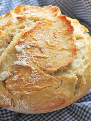 Crusty loaf of round bread on a blue-checked cloth