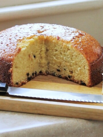 Cake on a cutting board with a slice out of it, the cutting knife next to it.