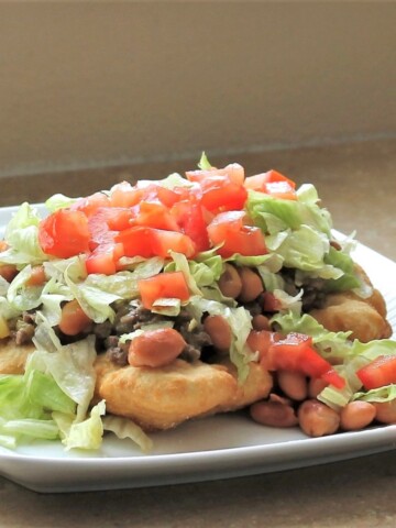 White plate with fry bread loaded with beans, beef, lettuce and tomato.