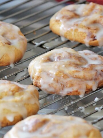 Big cinnamon roll cookies on a cooling rack, dripping with glaze.