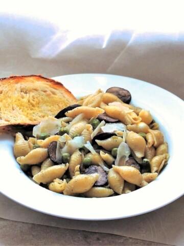 Big white bowl filled with shell pasta, mushrooms and parmesan, along with a slice of garlic toast.
