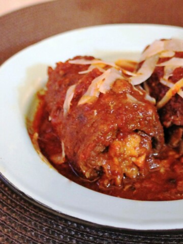 White bowl with two pieces of braised beef, smothered in marinara and sprinkled with fresh parmesan.
