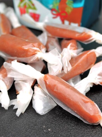 Homemade caramels wrapped in waxed paper next to a holiday box.