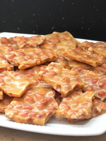 White plate full of golden brown brittle, full of peanuts.