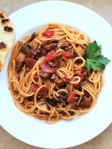 Overhead view of pasta with tomato and pasta sauce in a white bowl with a slice of bread on the side.