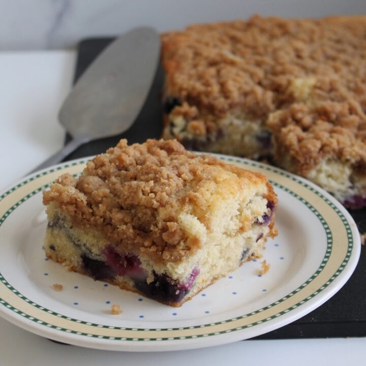 Slice of sour cream-blueberry crumb cake on a yellow-rimmed plate with a serving knife.