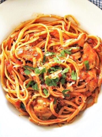 White bowl of pasta with artichokes and red sauce.