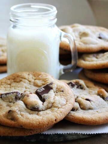 A pile of chewy chocolate chip cookies and a small glass of milk.
