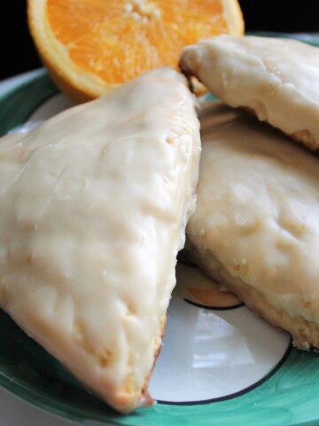 Three orange scones with orange glaze on a green plate.