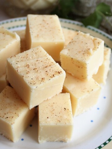 Eggnog Fudge stacked on a festive plate, sprinkled with fresh nutmeg.