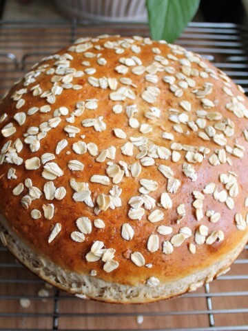 Big, golden browned loaf of oatmeal bread sprinkled with oatmeal flakes.