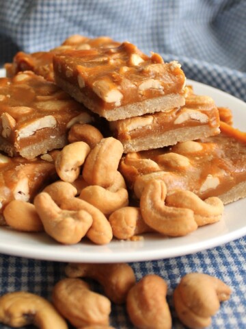 Butterscotch cashew shortbread bars on a white plate surrounded by fresh salted cashews.