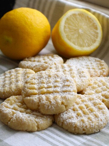 Soft lemon cookies with fresh lemons in the backgroun.