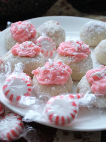 Little round peppermint cookies coated with powdered sugar. Peppermint candies around a white plate.