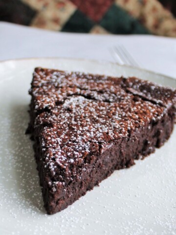 Deep chocolate slice of cake on a white plate.