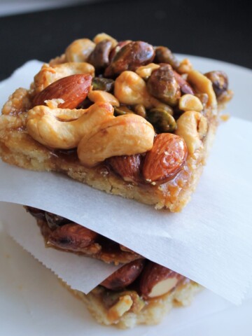 Nut bars stacked on a white plate with parchment between each bar.