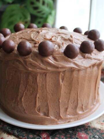 Malted Milk Cake with malt balls around the top, sitting on a white plate.