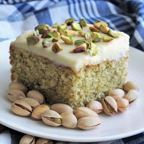 Piece of pistachio cake on a white plate with a blue-checked background.