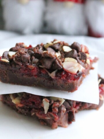 Close up of stacked chocolate cherry bars on a white plate with slips of parchment paper between slices.