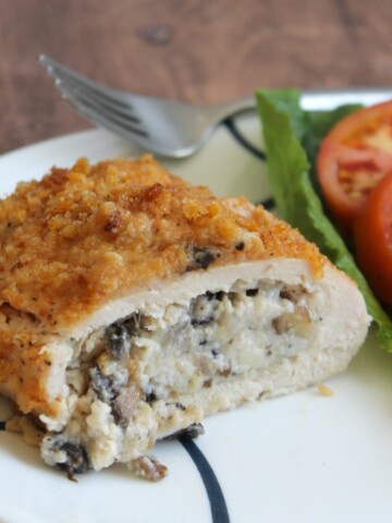 Piece of stuffed chicken breast with a side of sliced fresh tomatoes on a green lettuce leaf.
