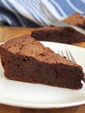 Slice of dense, rich chocolate cake on a white plate with a fork.