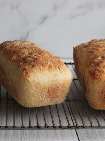 Two full loaves of English Muffin Bread on a wire racking, cooling.