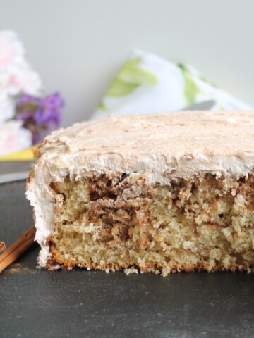 Snickerdoodle cake, cut and on a black cutting board with cinnamon sticks to the side.