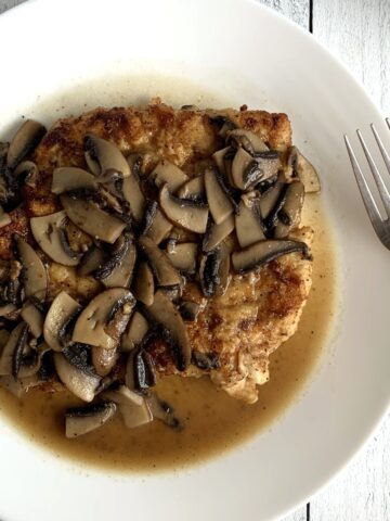 Close up of chicken smothered with mushrooms and a buttery white wine sauce.