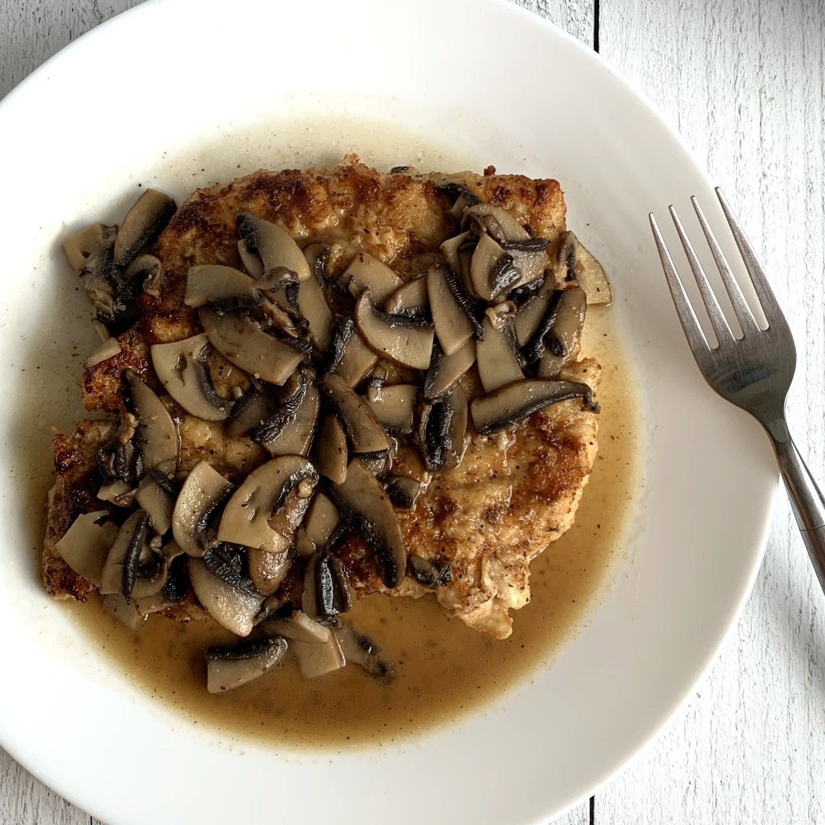 Close up of chicken smothered with mushrooms and a buttery white wine sauce.